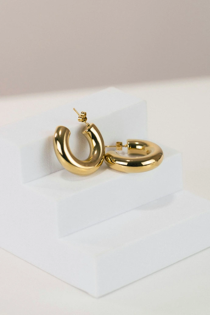 a pair of gold hoop earrings on a white stand