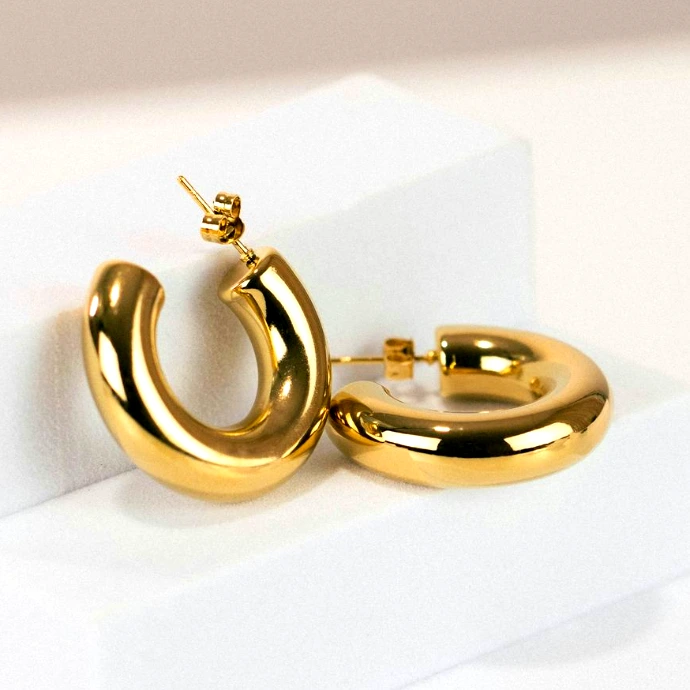 a pair of gold hoop earrings on a white stand